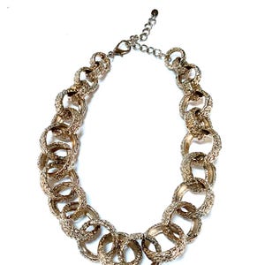 Puede incluir: Collar dorado con grandes anillos texturizados entrelazados. El collar tiene una extensi&oacute;n de cadena para ajustar la longitud y un cierre de mosquet&oacute;n. El dise&ntilde;o es audaz y llamativo, adecuado para cualquier atuendo.