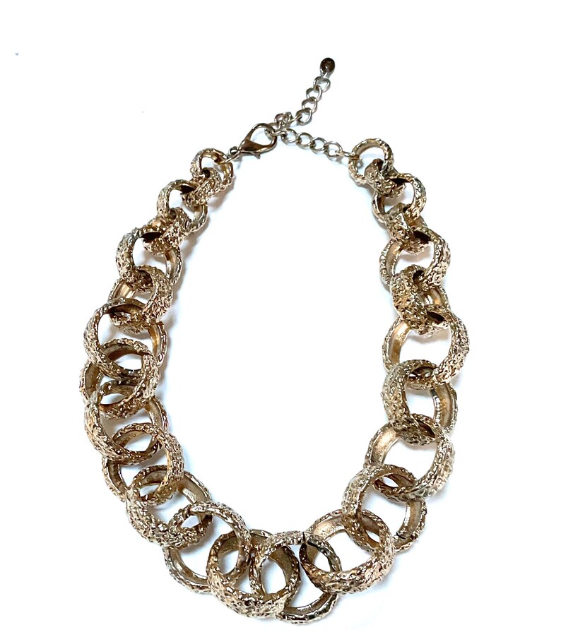 Puede incluir: Collar dorado con grandes anillos texturizados entrelazados. El collar tiene una extensi&oacute;n de cadena para ajustar la longitud y un cierre de mosquet&oacute;n. El dise&ntilde;o es audaz y llamativo, adecuado para cualquier atuendo.