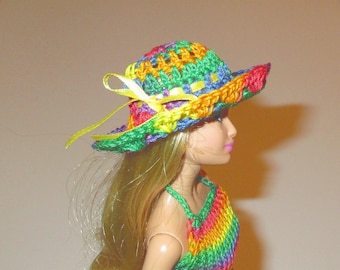 May include: A doll wearing a multicolored crochet hat and a matching rainbow-striped crochet top. The hat features a vibrant pattern of green, orange, yellow, and blue yarn with a thin yellow ribbon tied in a bow on the side of the brim.