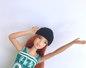 May include: A red-haired doll wearing a black beanie and a teal and green tank top with the text "GLA" on it.