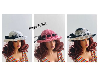 May include: Three crocheted hats in white, pink, and black and white. The hats are shown on a doll with long brown hair and a striped shirt. The text "Happy To Knit" is visible in the image.