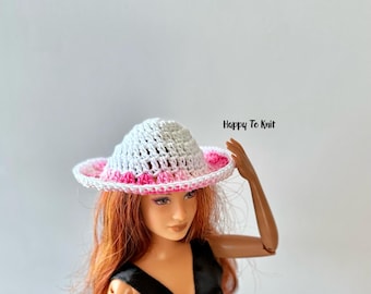 May include: A white and pink crochet hat with a wide brim. The hat has a white crown and a pink and white brim. The text "Happy To Knit" is in the upper right corner. The hat is on a doll.