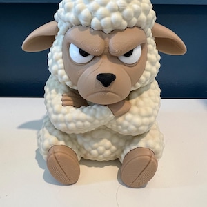May include: A 3D printed figurine of a sheep with a textured, cream-colored wool coat and a tan face. The sheep has a grumpy facial expression with furrowed brows, white eyes with black pupils, and arms crossed over its chest while sitting.