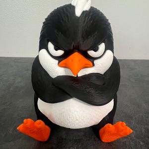 May include: A three-dimensional penguin figurine with black and white coloring, featuring a bright orange beak and feet. The penguin has a grumpy facial expression with furrowed brows and its wings are crossed over its chest.