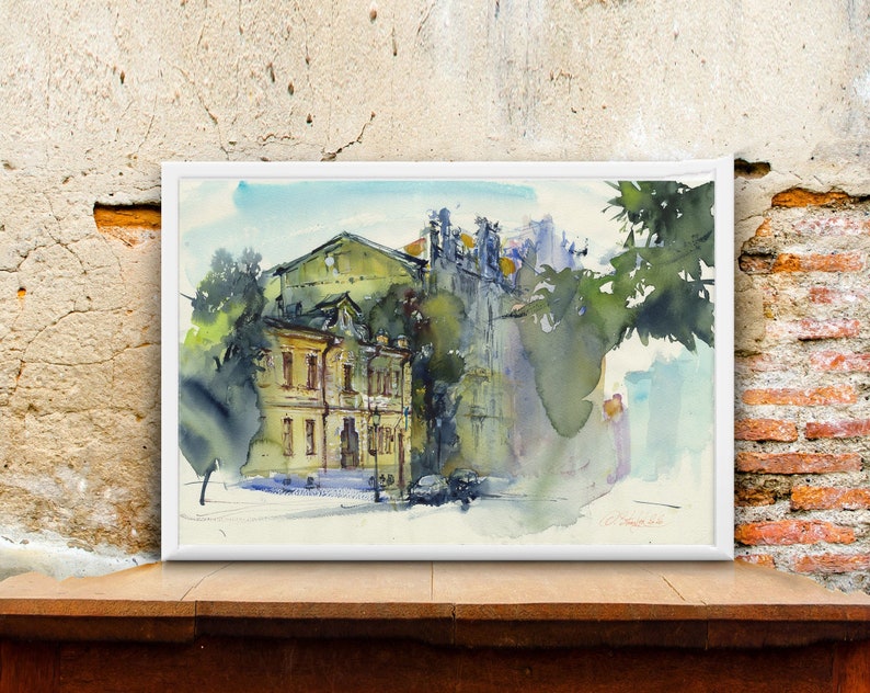 May include: Watercolor painting of a yellow building with a green roof and trees in the foreground. The building has windows and a door. The painting is framed in white.