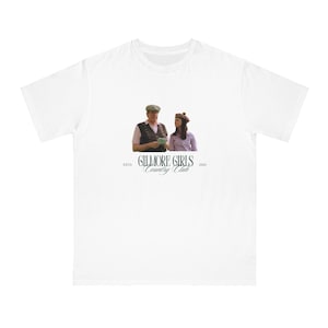 May include: White t-shirt featuring a still from the TV show Gilmore Girls. The image shows two people with the text "GILMORE GIRLS Country Club" and the year "2000". The shirt has a crew neck and short sleeves.