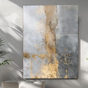 Può includere: Opera d'arte astratta da parete con un aspetto strutturato e invecchiato. L'opera presenta una miscela di toni grigi, oro e marrone, creando un'estetica moderna e artistica. Il pezzo è esposto sopra un divano letto con cuscini, piante e un pouf intrecciato.