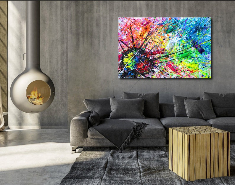 May include: Abstract painting with a colorful splatter design in shades of blue, green, yellow, red, and black. The painting is displayed on a wall above a gray couch and a wooden coffee table.