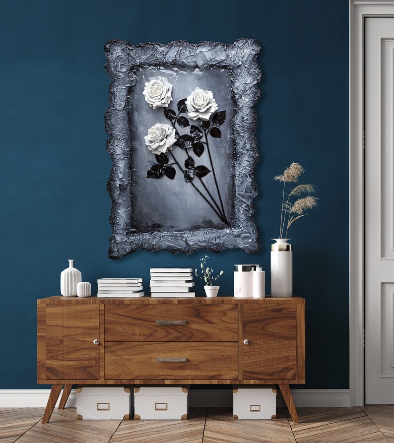 May include: A framed painting of three white roses with black stems and leaves on a gray background. The frame is textured and has a distressed look.