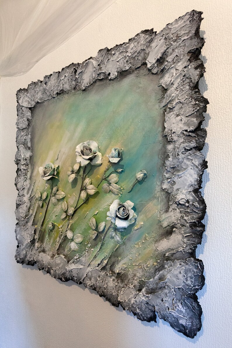 May include: A textured, gray frame surrounds a painting of white roses on a green and blue background. The roses are sculpted and appear to be three-dimensional.