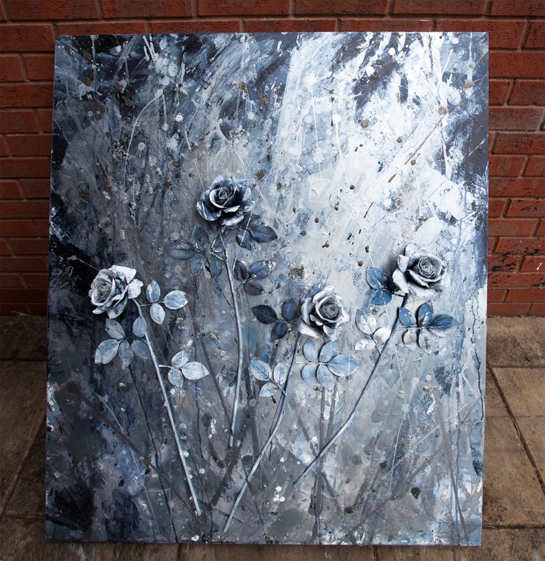 May include: A square abstract painting with raised grey roses and blue-grey leaves and stems. The background is a textured mix of grey, white, and silver paint. The artwork is mounted on a wooden frame, creating a three-dimensional effect.