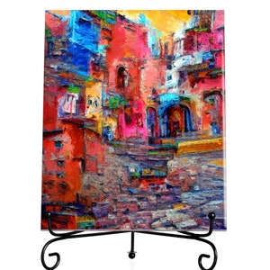 Pode incluir: Uma pintura abstrata colorida de uma cidade com edifícios em tons de vermelho, azul, amarelo e rosa. A pintura está em um cavalete preto.