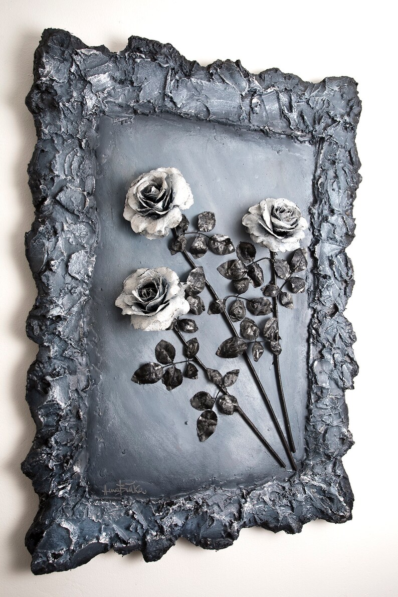 May include: A black and white framed wall art piece featuring three silver roses with black stems and leaves. The frame is textured and has a rough, uneven surface.
