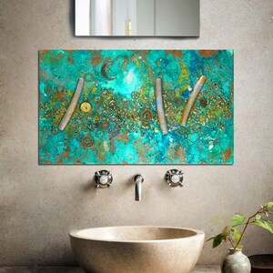 May include: A turquoise and gold abstract art piece with a textured surface. The art piece features a design of gears and metal strips. The art piece is hanging on a wall above a sink in a bathroom.