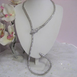 May include: A silver snake-shaped necklace with clear rhinestones. The necklace is on a white mannequin bust.