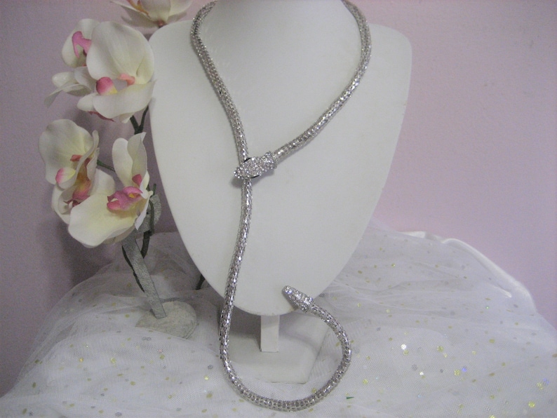 May include: A silver snake-shaped necklace with clear rhinestones. The necklace is on a white mannequin bust.