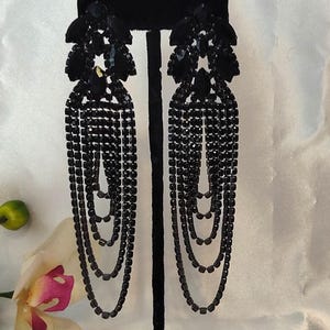 May include: Elegant black chandelier earrings with a floral design at the top and multiple cascading strands of small, dark beads. The earrings are displayed on a black stand against a white background.