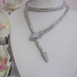 May include: A silver snake-shaped necklace with a crystal-encrusted head. The necklace is on a white mannequin bust.