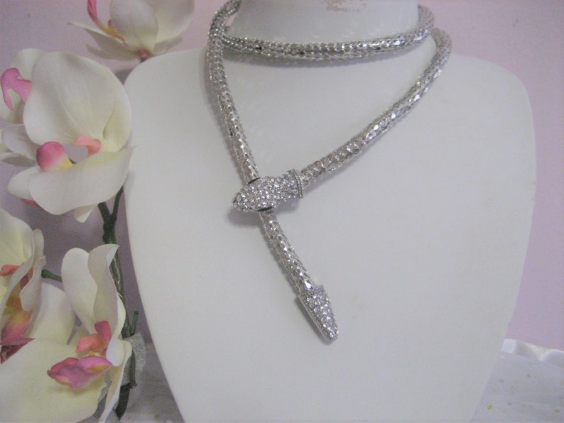 May include: A silver snake-shaped necklace with a crystal-encrusted head. The necklace is on a white mannequin bust.