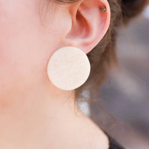 May include: A pair of large, round, white earrings. The earrings are made of a smooth, textured material.