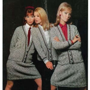 Puede incluir: Tres mujeres con trajes de falda de tweed gris a juego con ribetes y botones negros. Cada atuendo incluye una rebeca, una falda y una camisa con cuello. Una mujer lleva una corbata roja, otra una camisa roja y la tercera una camisa blanca.