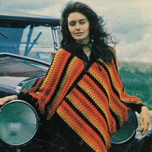 May include: A colorful crochet poncho with orange, yellow, and black stripes. The poncho has a fringed hem and is worn over a black top. The image has a vintage aesthetic, with a classic car in the background.