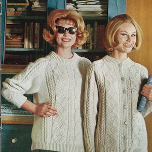 May include: Two women wearing matching cream-colored cable-knit sweaters. One sweater is a crew neck, and the other is a cardigan with buttons. The woman on the left is wearing sunglasses. They are standing in front of a teal cabinet.