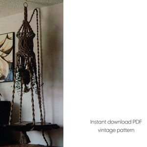 May include: A brown macrame plant hanger with a wooden shelf, suspended from a ceiling hook. The design includes intricate knotting and a lower shelf for displaying plants. The text "Instant download PDF vintage pattern" is visible.