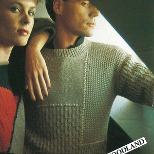 May include: A light green knit sweater with a textured design. The sweater has a crew neck and a patchwork design on the front. The sleeve has a patterned design. The word "WOODLAND" is in the bottom right corner.