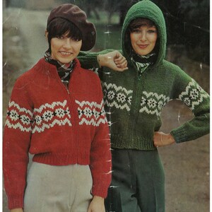 May include: Two women wearing knitted sweaters with a geometric pattern. The sweater on the left is red with white and black accents. The sweater on the right is green with white and black accents. The sweater on the right has a hood. The sweaters are labeled "Patons 1392 Husky 32-40 in 81-102 cm."
