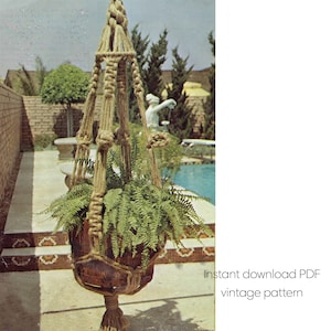 Op de afbeelding: Een vintage macramé plantenbak met een houten pot gevuld met groene varens. De plantenbak is opgehangen aan een geknoopt touw, met een retro design. De afbeelding bevat de tekst "Instant download PDF vintage pattern".
