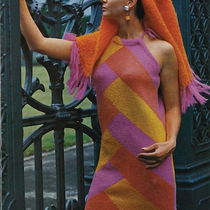 May include: A retro image of a woman in a colourful geometric dress. The dress is a halterneck style with diagonal stripes in pink, orange, and yellow. She wears an orange shawl with pink fringe.