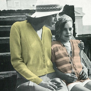 May include: A woman and child are seated outdoors, both wearing knit cardigans. The woman's cardigan is a light yellow, button-down style. The child's cardigan is striped in shades of orange and brown. The woman wears a white hat with a patterned band.