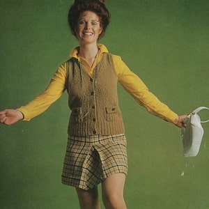 May include: A woman wearing a yellow collared shirt, a brown knitted vest, and a plaid skirt. She is holding a white purse. The background is a solid green color.