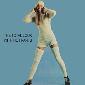 May include: A retro fashion image showing a woman in a cream-coloured knitted outfit. The ensemble comprises a turtleneck sweater, shorts, a beanie hat, and thigh-high socks. The text "THE TOTAL LOOK WITH HOT PANTS" is visible against a blue backdrop.