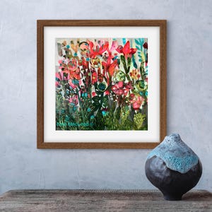 Pode incluir: Uma pintura abstrata emoldurada de um arranjo floral colorido com tons de vermelho, rosa, verde e azul. A pintura está em uma moldura marrom e está sobre uma mesa de madeira.