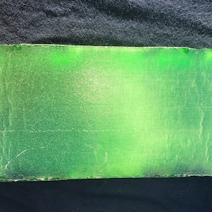 May include: A large, rectangular slab of green glass with a smooth, polished surface. The glass has a slight green tint and is translucent.