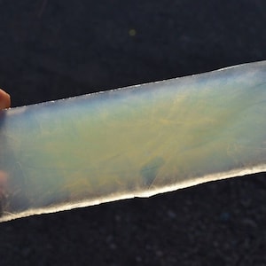 May include: A translucent, rectangular piece of opal with a light blue and yellow hue. The opal is smooth and has a slight sheen.