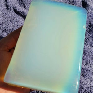 May include: A large, rectangular piece of polished opal with a milky white color and iridescent rainbow sheen.