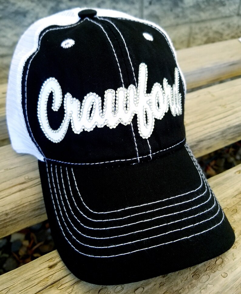 May include: Black and white trucker hat with a white mesh back and a white embroidered "Crawford" on the front. The hat has a black brim with white stitching.