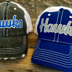 Puede incluir: Dos gorras de camionero con la palabra "Hawks" bordada en la parte delantera. Una gorra es negra con malla blanca y letras azules. La otra gorra es azul con malla blanca y letras plateadas.