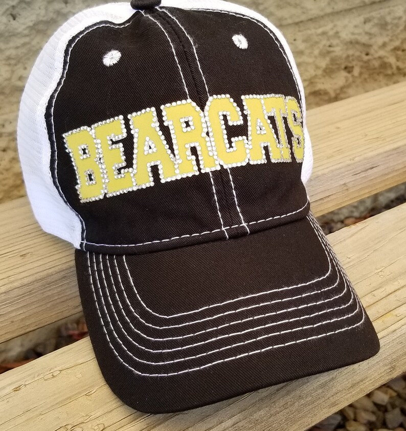 May include: A black baseball cap with a white mesh back and white stitching. The front panel features the word BEARCATS in gold lettering outlined with small clear rhinestones. The cap has a curved brim and a button on the top center.