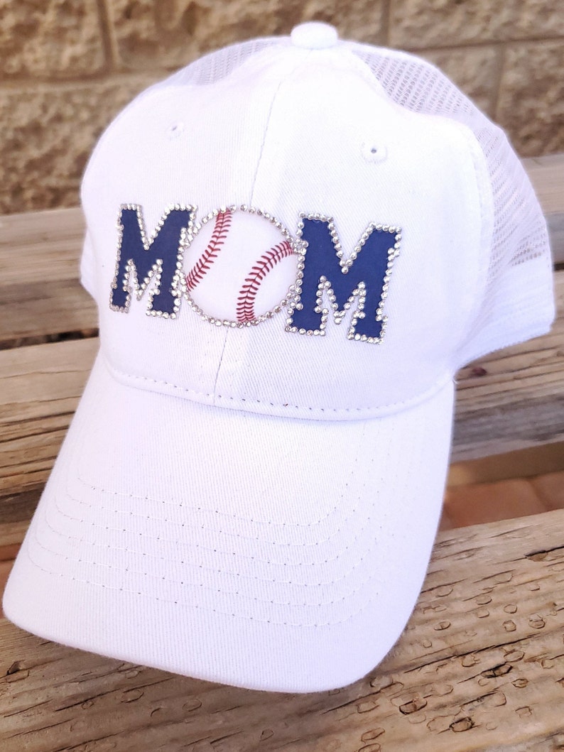May include: White baseball cap with a blue and white rhinestone MOM design and a baseball graphic.