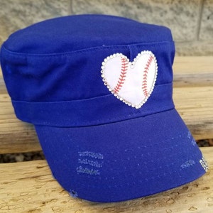 Pode incluir: Bon&eacute; azul royal de estilo militar com aba desgastada. Um patch branco em forma de cora&ccedil;&atilde;o, semelhante a uma bola de beisebol, &eacute; adornado com costuras vermelhas e rodeado por strass. Este acess&oacute;rio &eacute; elegante.