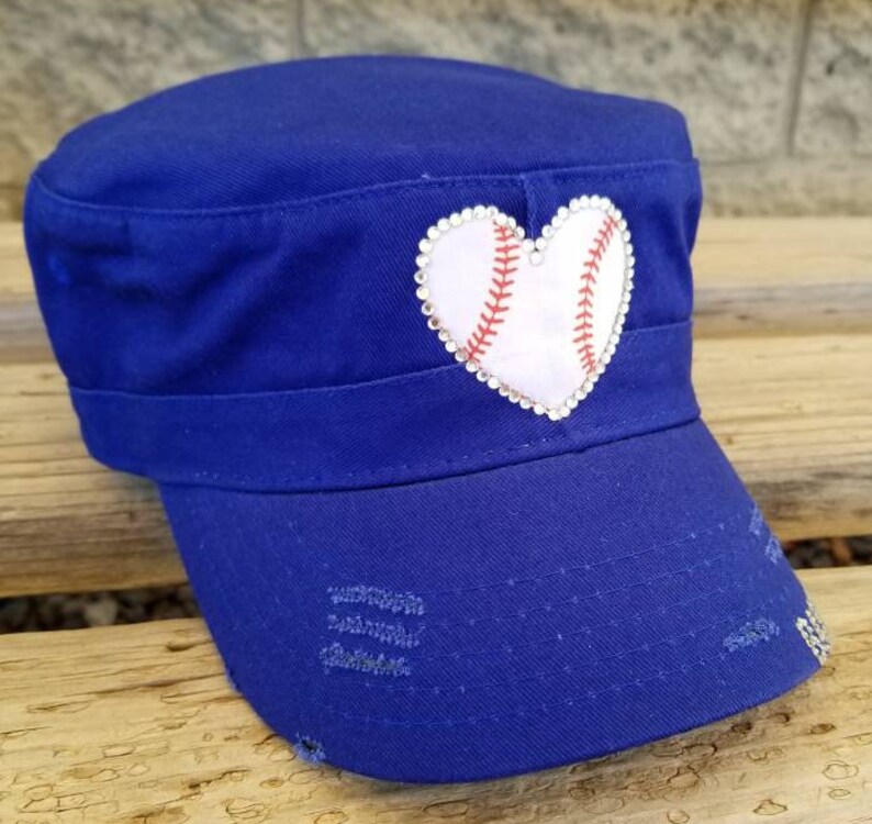 Pode incluir: Bon&eacute; azul royal de estilo militar com aba desgastada. Um patch branco em forma de cora&ccedil;&atilde;o, semelhante a uma bola de beisebol, &eacute; adornado com costuras vermelhas e rodeado por strass. Este acess&oacute;rio &eacute; elegante.