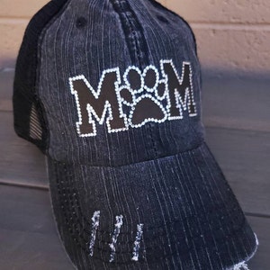 May include: Black and grey distressed baseball cap with a black paw print and the word "MOM" in rhinestones.