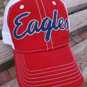May include: Red and white baseball cap with a navy blue "Eagles" logo with rhinestones. The cap has a mesh back.