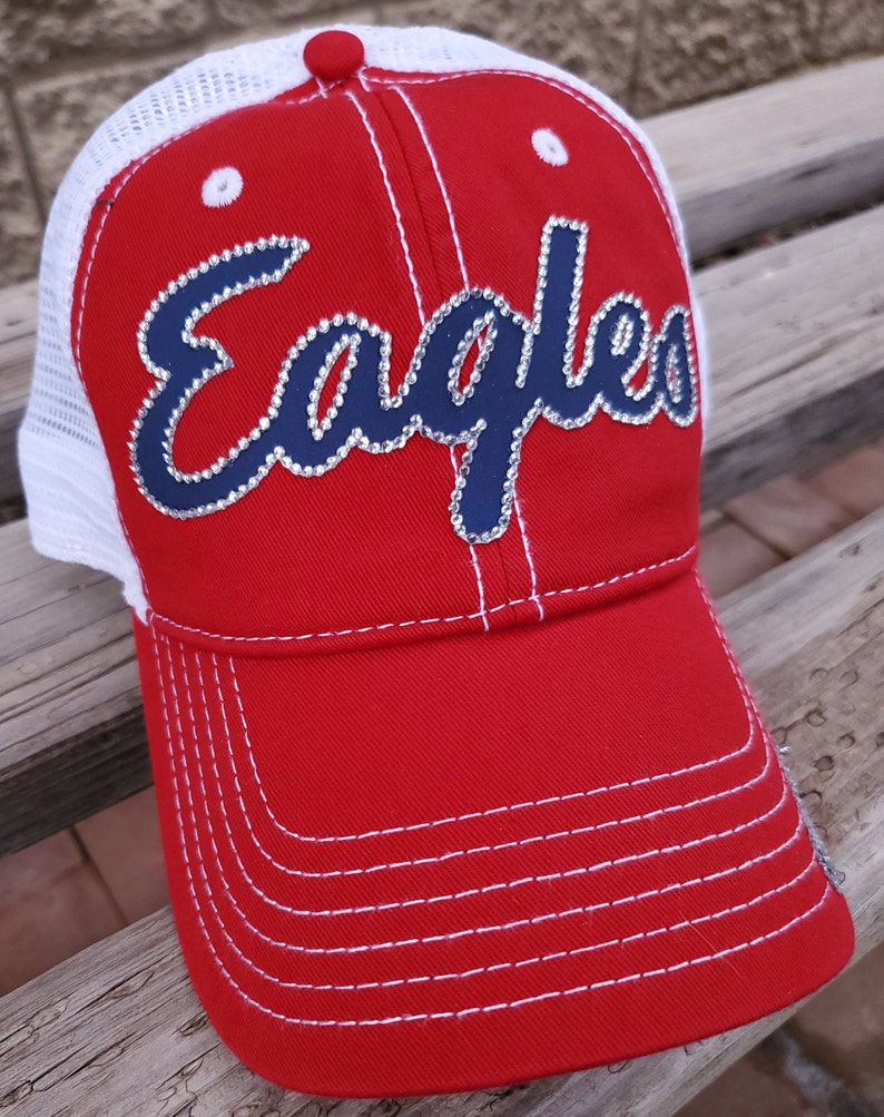 May include: Red and white baseball cap with a navy blue "Eagles" logo with rhinestones. The cap has a mesh back.