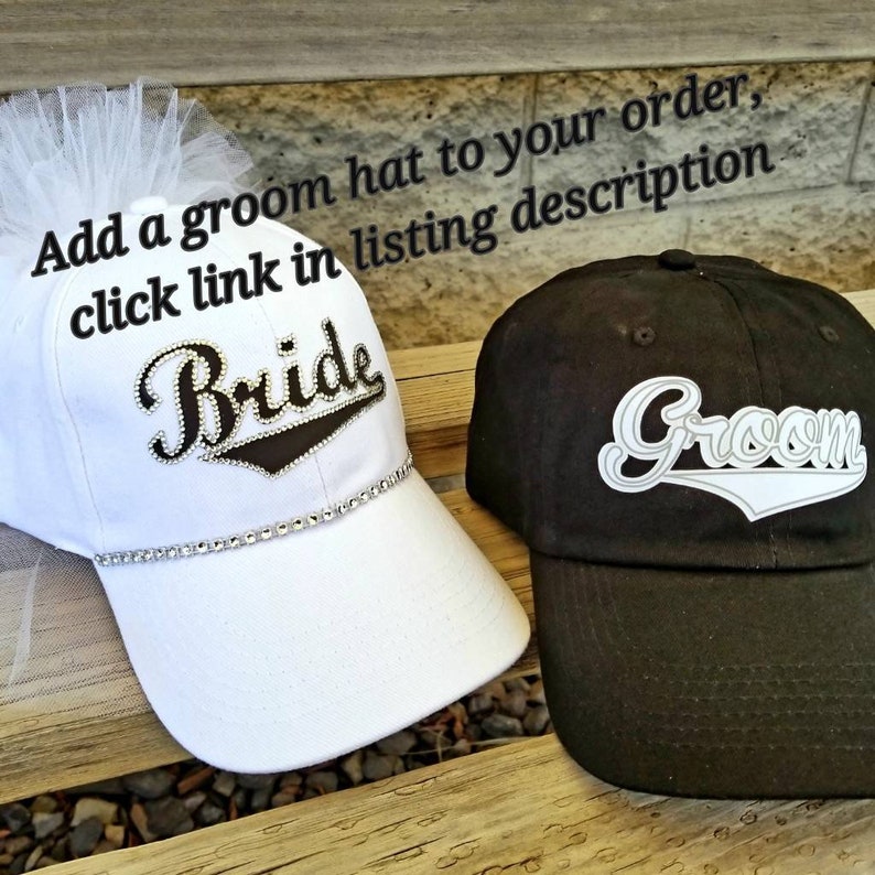 May include: Two baseball caps, one white with a tulle veil and the word "Bride" in rhinestones, the other black with the word "Groom" in white.