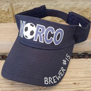 May include: A black visor with a white soccer ball and the word "WORCO" in rhinestones. The visor also has the text "Brewer #15" in rhinestones.